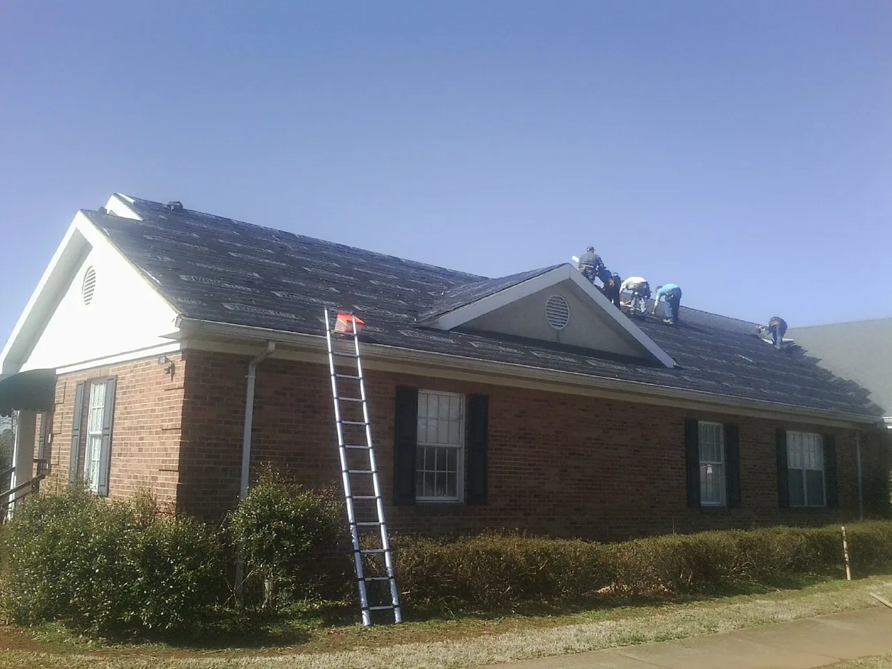 Crew tearing shingles off a brick ranch roof with a ladder set — Emergency Roof Repair work by our crew in Harlan