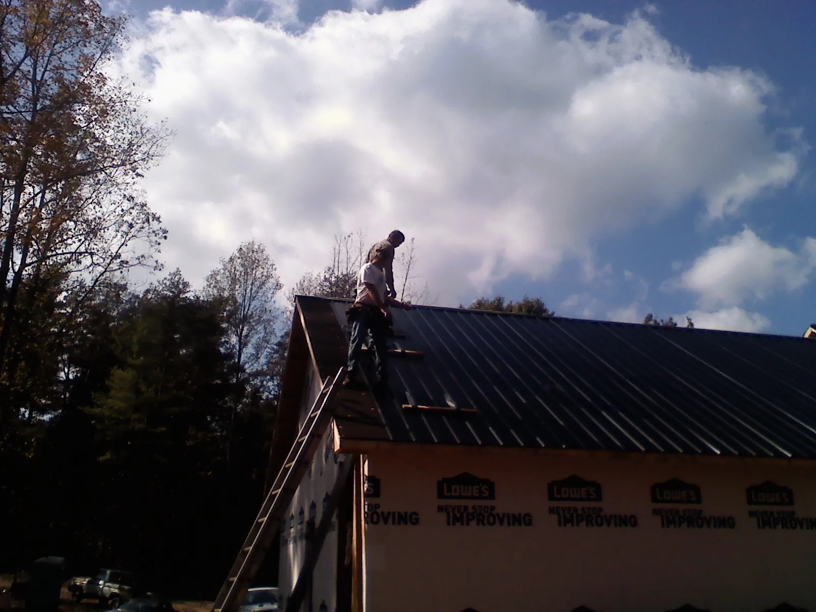 Roofer fastening dark metal panels high against a cloudy sky, from a Roof Inspection job in Harlan
