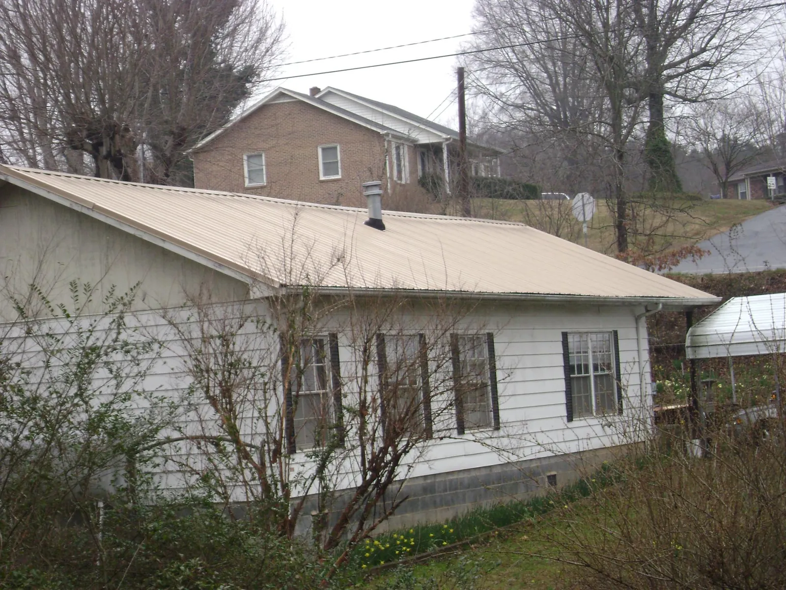 Tan metal roof on a white sided house set into a hillside — Commercial Roofing by Roofing Brothers in Harlan