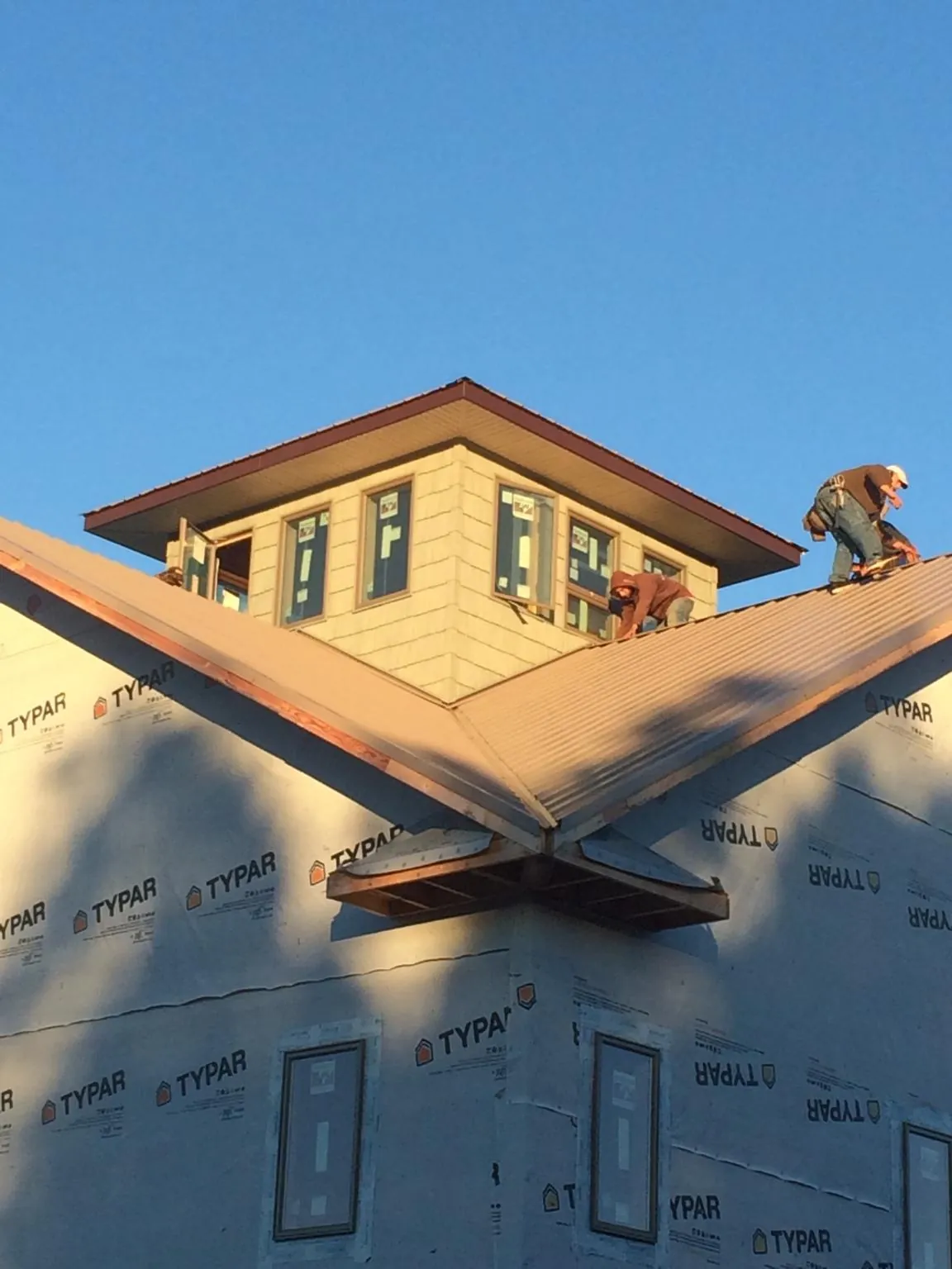 Roofers working around a rooftop cupola on a new metal roof at sunset — Roof Waterproofing in Harlan by Roofing Brothers